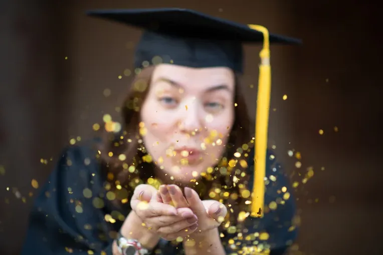 Graduating Student blowing gold confetti