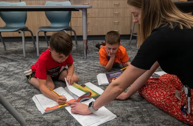 Two students reading a book with the help of a teacher